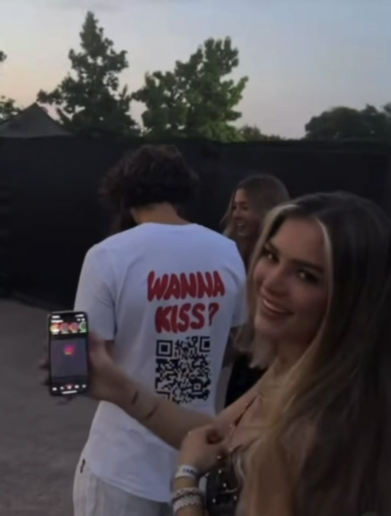 Person wearing the wanna kiss? tee with a QR code in a neon-lit bar